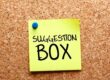 Post-it sur un tableau en liège avec écrit "Boite à suggestions" dessus
