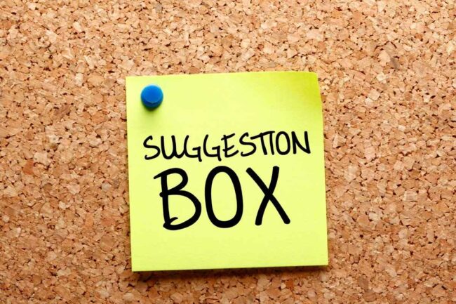 Post-it sur un tableau en liège avec écrit "Boite à suggestions" dessus